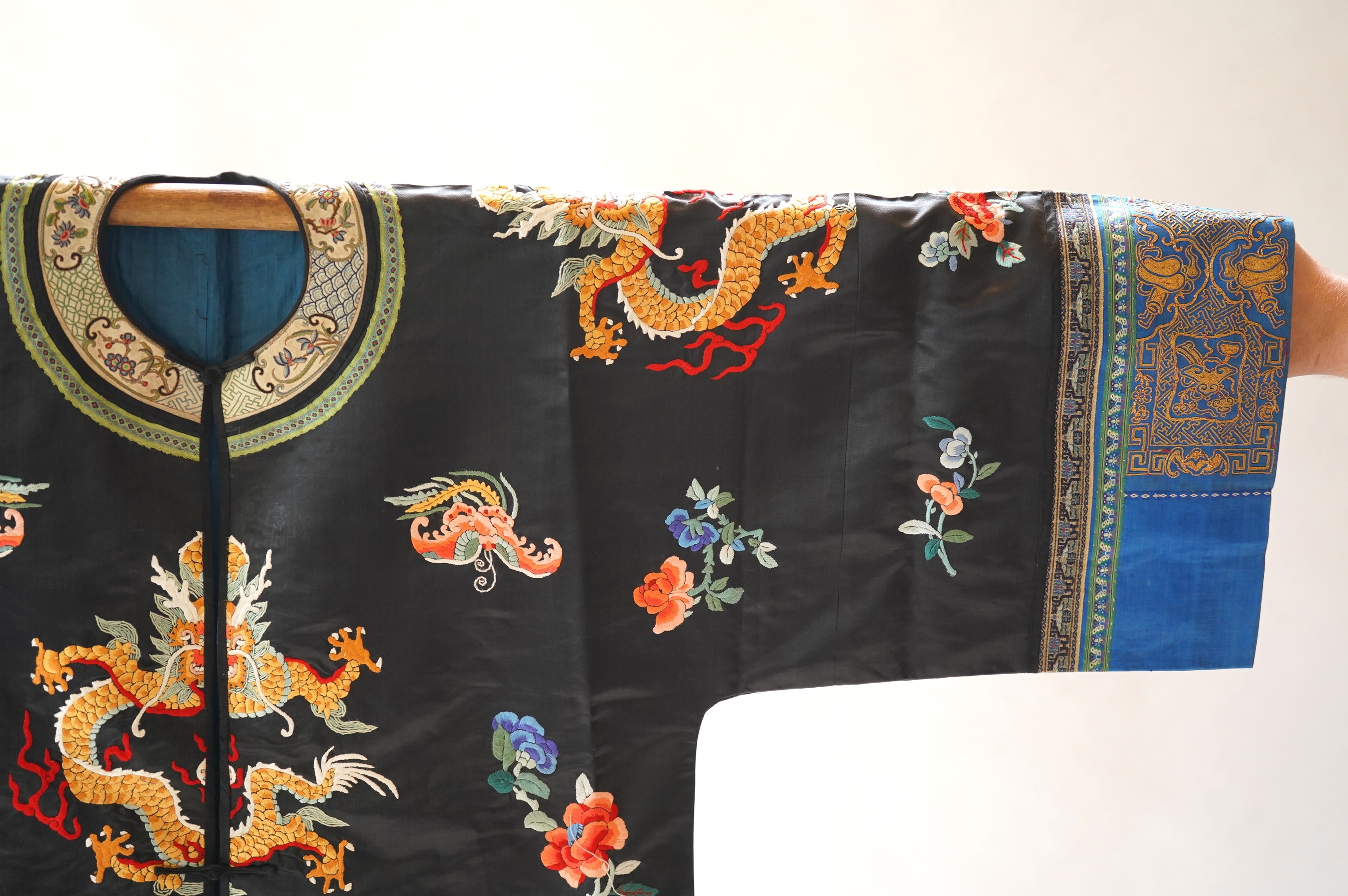 An early 20th century Chinese blue satin silk embroidered dragon robe, embroidered with five claw dragon symbols with flaming pearls, surrounded by bats and flower motifs, with gold thread embroidered dragon sleeve bands